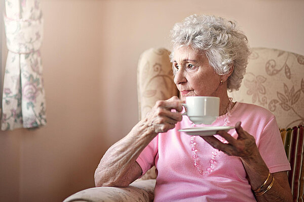 An elderly lady smiling whilst holding a cup of tea.